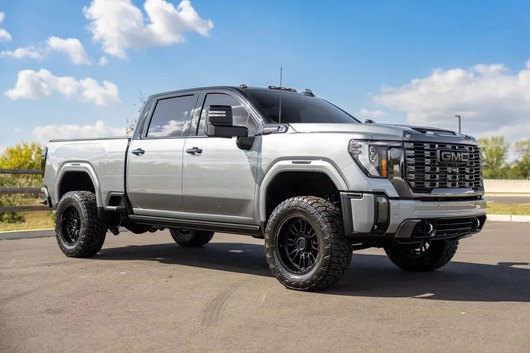A black 2024 GMC Sierra 2500 Denali Ultimate with a lift kit, tuxedo wrap, and chrome accents parked outdoors.