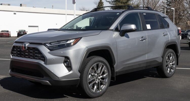 A silver Toyota RAV4 with a roof rack parked in a parking lot. The RAV4 is a popular SUV known for its reliability, fuel efficiency, and cargo space