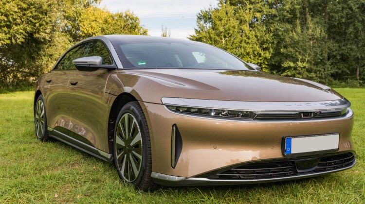 A silver Lucid Air electric car parked in a field. The Lucid Air is a luxury sedan with a spacious interior and a long driving range