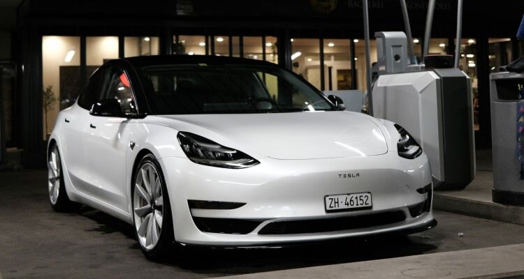 A white Tesla Model 3 charging at a charging station. The Tesla Model 3 is an electric car known for its long range, performance, and sleek design